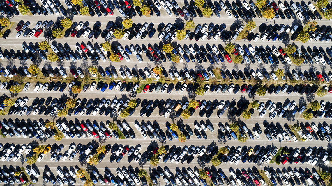A large parking lot with rows of cars and green trees viewed from above.